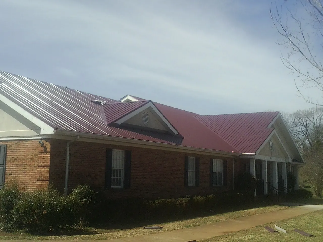 Red metal roof with gabled entries on a long brick building, from a Hail Damage Roof Repair job in Robins