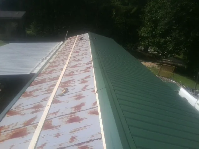 Old rusted panels beside newly installed green metal roofing — Wind Damage Roof Repair by Roofing Brothers in Robins