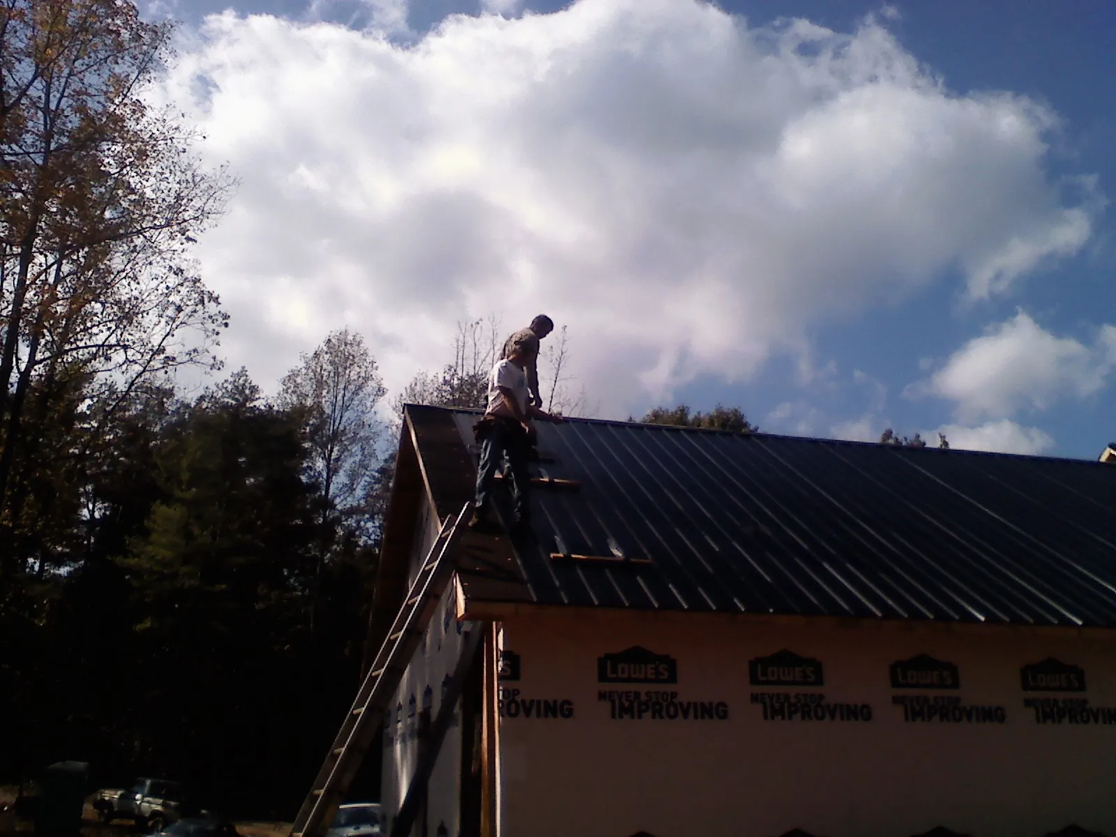 Roofer fastening dark metal panels high against a cloudy sky, from a Roof Inspection job in Robins