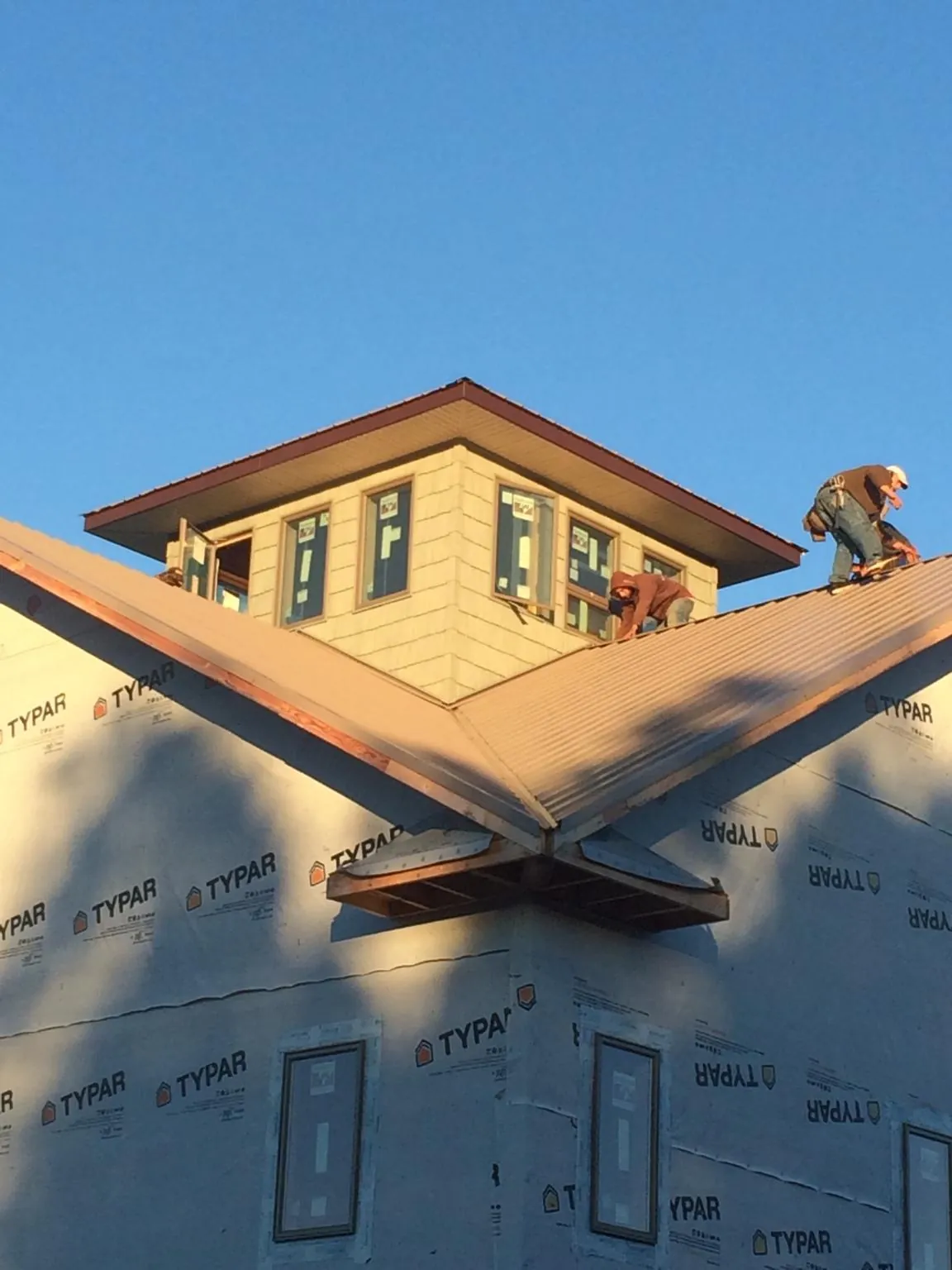 Roofers working around a rooftop cupola on a new metal roof at sunset — Roof Waterproofing in Robins by Roofing Brothers